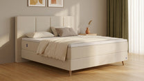 Bruno Boxspringbett mit Vertica-Kopfteil, in Beige, Winkelansicht, im Wohnraum, mit Topper, mit Füßen aus nordischer Eiche